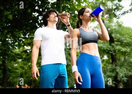 Giovane beve l'acqua dopo il jogging per rifornire di energia e di idrato Foto Stock