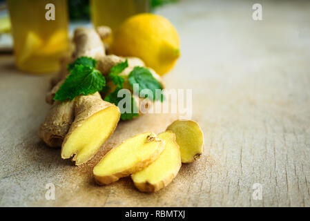 Ingredienti per lo zenzero detox acqua. Radice di Zenzero, limone e melissa su sfondo di legno Foto Stock