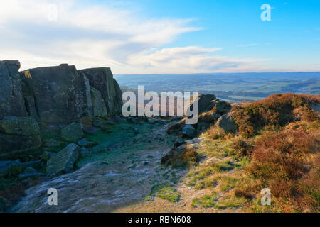 La brina si trova sul terreno nell'ombra di una piccola scogliera gritstone sul bordo Curbar Foto Stock