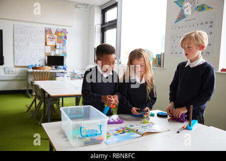 Una ragazza e due ragazzi in piedi in una tabella in una scuola primaria classe lavorando insieme con il giocattolo di blocchi di costruzione Foto Stock