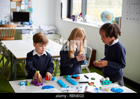 Vista in elevazione dei tre scuola primaria i bambini lavorano insieme utilizzando blocchi di costruzione in una classe Foto Stock