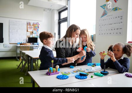 Femmina di insegnante di scuola primaria seduta a tavola con i bambini in una classe, lavorare insieme con il giocattolo di blocchi di costruzione Foto Stock