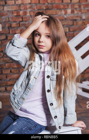 Ritratto poco fashion kid.elegante ragazza parigamba bambino indossando giacca denim,jeans abiti,ponendo ruvida contro un muro di mattoni. guarda fiducioso,ribelle.bella faccia bambini caucasici's,fashion concept. Foto Stock