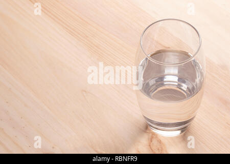 Immagine di un mezzo bicchiere pieno di acqua in piedi su un tavolo di legno Foto Stock