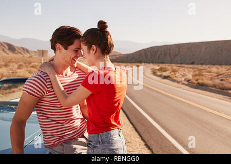 Bianco giovane coppia abbracciando con le loro auto in strada Foto Stock