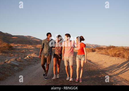 Due giovani coppie di adulti a camminare su una strada nel deserto Foto Stock