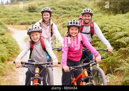 Ritratto di genitori e bambini seduti sulle mountain bike in un vicolo del paese durante una famiglia viaggio di campeggio, vista frontale Foto Stock