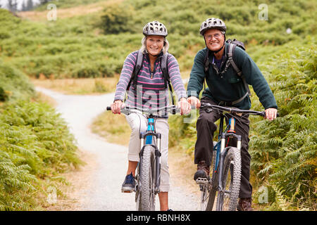 Coppia senior seduti sulle mountain bike in un vicolo del paese durante una vacanza in campeggio, guardando la telecamera, vista frontale Foto Stock