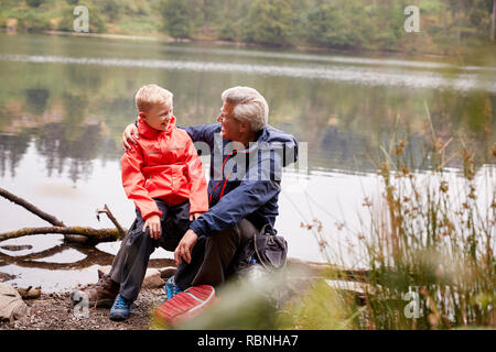 Nipote seduta sul suo nonno del ginocchio sulla riva di un lago, Lake District, REGNO UNITO Foto Stock