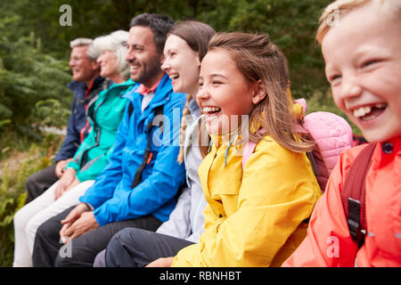 Vista laterale del multi generazione famiglia ammirando la vista seduti insieme sulla riva di un lago di ridere, il fuoco selettivo del Lake District, REGNO UNITO Foto Stock