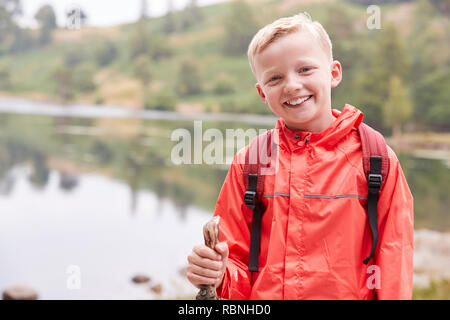 Un pre-teen boy in piedi sulla riva di un lago, cercando di fotocamera, vista frontale, vita, Lake District, REGNO UNITO Foto Stock