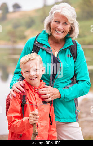 Nonna e nipote insieme in piedi vicino a un lago in campagna a sorridere alla telecamera, vicino Lake District, REGNO UNITO Foto Stock