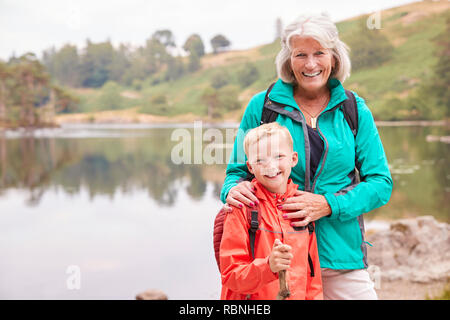 Nonna e nipote insieme in piedi vicino a un lago in campagna a sorridere alla telecamera, vicino Lake District, REGNO UNITO Foto Stock