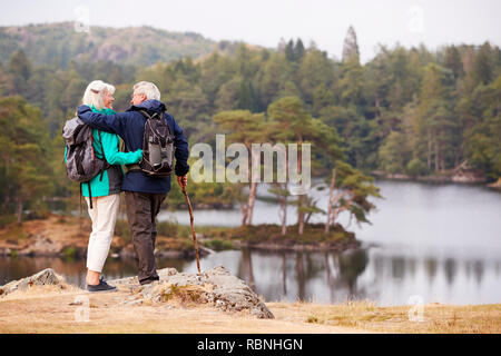 Coppia senior abbracciando e ammirando una vista di laghi guardando ogni altro, vista posteriore Foto Stock