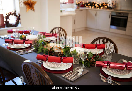 Tavola di natale con impostazione Christmas Cracker disposte su piastre in una sala da pranzo con cucina in background Foto Stock