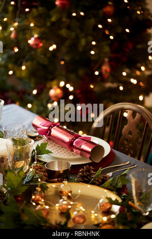 Tavola di Natale un impostazione con Christmas Cracker disposti su una piastra e la tabella decorazioni, un albero di Natale in background Foto Stock