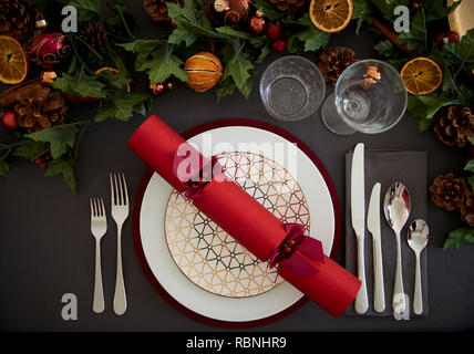 Tavola di Natale impostazione con un rosso Christmas Cracker disposti su di una piastra e di colore verde e rosso tabella decorazioni, vista aerea Foto Stock