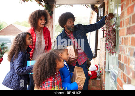 Famiglia a bussare alla porta anteriore come essi arrivano per visitare il giorno di Natale con doni Foto Stock