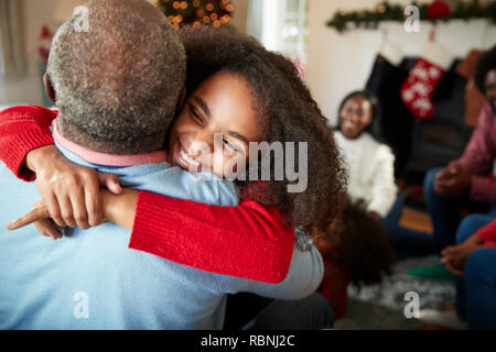 La nipote dando nonno abbraccio come Multi generazione Famiglia festeggiano il Natale a casa Foto Stock