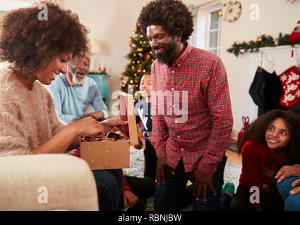 Giovane lo scambio di doni come Multi generazione Famiglia festeggiano il Natale a casa insieme Foto Stock