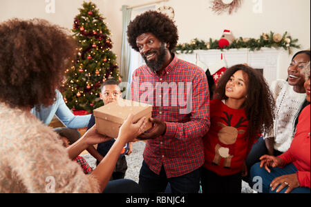 Giovane lo scambio di doni come Multi generazione Famiglia festeggiano il Natale a casa insieme Foto Stock