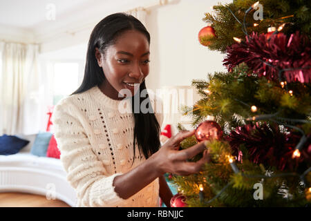 Donna appeso decorazioni su albero di Natale a casa Foto Stock