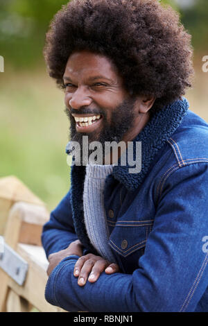 Uomo nero appoggiato su di una recinzione di legno in campagna a ridere, close up Foto Stock