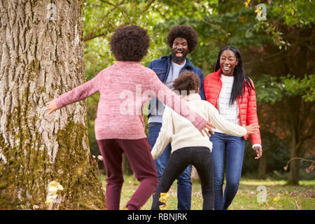 Due bambini che salta fuori da dietro un albero per cogliere di sorpresa i genitori durante una passeggiata nel parco, vista posteriore Foto Stock