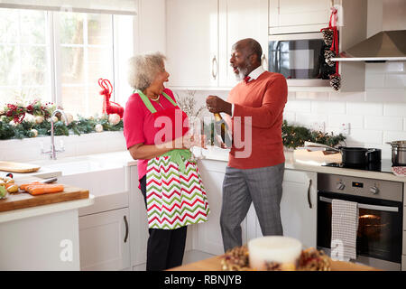 Senior coppia nero apertura champagne e ridere insieme in cucina mentre si prepara la cena il giorno di Natale, il fuoco selettivo Foto Stock