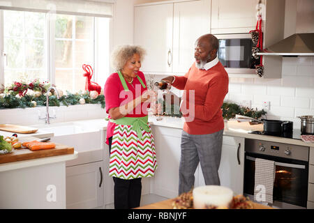 Senior uomo nero versando champagne per il suo partner in cucina mentre si prepara la cena il giorno di Natale, il fuoco selettivo Foto Stock