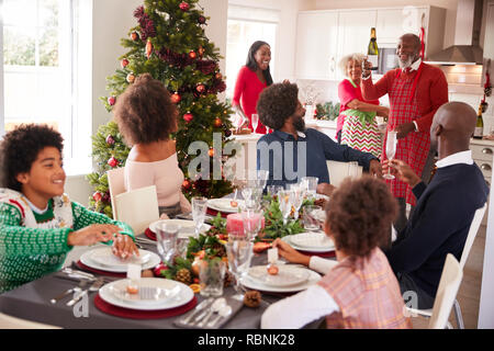 Razza mista, multi generazione incontro di famiglia nella sala da pranzo di sedersi intorno a un tavolo per la cena di Natale, nonno tenendo la bottiglia di champagne Foto Stock