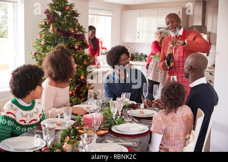 Nonno nero apertura champagne per la sua generazione multi family, riuniti nella sala da pranzo per la cena di Natale Foto Stock