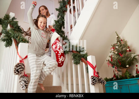 Famiglia eccitato indossando pigiami correndo giù per le scale tenendo le calze sulla mattina di Natale Foto Stock