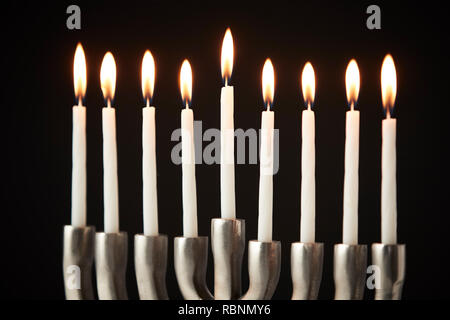 Candele accese sul metallo Hanukkah Menorah contro il nero di sfondo per studio Foto Stock