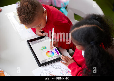 Vista in elevazione di due kindergarten scuola i bambini seduti ad una scrivania in un disegno in aula con un computer tablet e stilo, close up Foto Stock