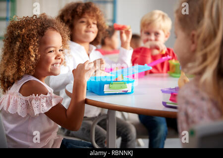 Close up di sorridere i giovani bambini seduti ad un tavolo a mangiare il loro pranzo al sacco insieme alla scuola infantile, il fuoco selettivo Foto Stock