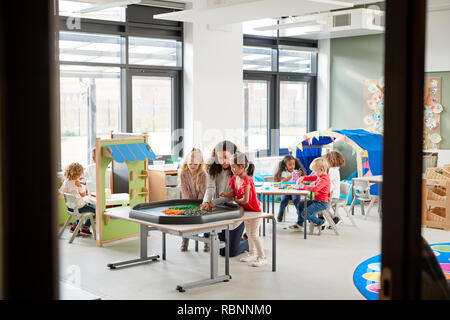 I bambini giocando con una femmina di insegnante in una classe in una scuola infantile, visto dalla porta Foto Stock