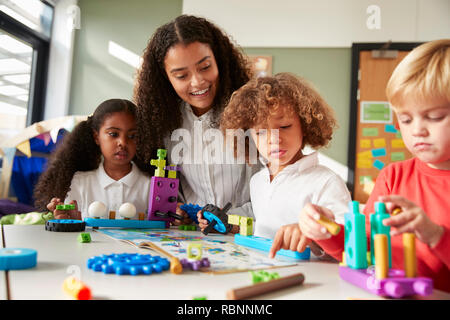 Insegnante femmina seduti al tavolo nella sala da gioco con tre bambini kindergartne costruzione, messa a fuoco selettiva Foto Stock