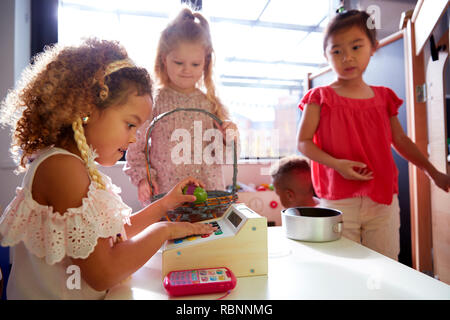 Tre studentesse kindergarten riproduzione di negozio in una playhouse presso una scuola infantile, retroilluminato Foto Stock