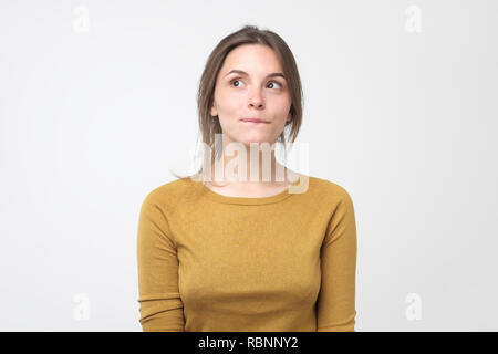 Giovane donna difficile avere qualcosa in mente con sly espressioni facciali, su sfondo grigio Foto Stock
