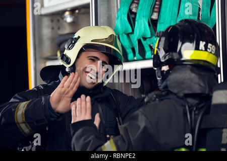 Foto di due vigili del fuoco gli uomini rendendo stretta di mano in prossimità di fuoco carrello Foto Stock