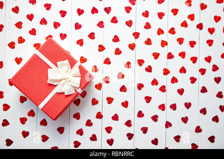 Regalo confezionato posto su a forma di cuore di paillettes rosso su bianco tavolo in legno Foto Stock