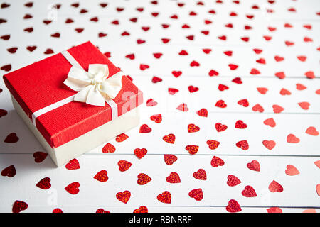 Regalo confezionato posto su a forma di cuore di paillettes rosso su bianco tavolo in legno Foto Stock