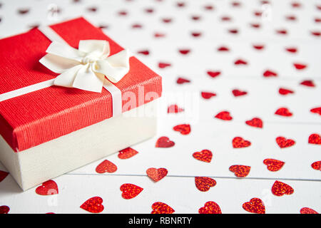 Regalo confezionato posto su a forma di cuore di paillettes rosso su bianco tavolo in legno Foto Stock