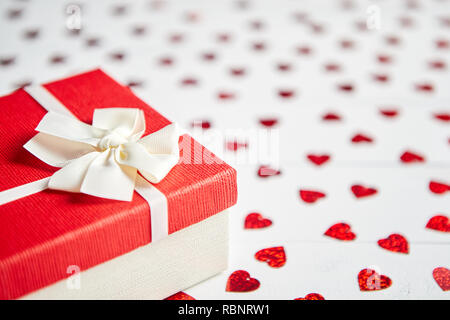 Regalo confezionato posto su a forma di cuore di paillettes rosso su bianco tavolo in legno Foto Stock