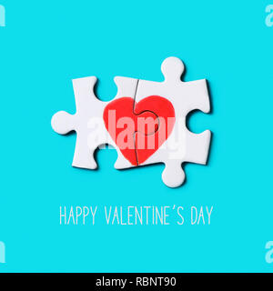 Primo piano di due pezzi di un puzzle formando un cuore e il testo happy valentines day su uno sfondo blu Foto Stock