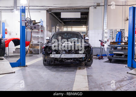 Smontaggio nero auto in officina vicino all'ascensore vetture preparate per la riparazione: estremità anteriore, il cofano e il paraurti staccato, attrezzature interne, pezzi di ricambio e Foto Stock