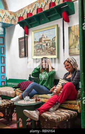 Due ragazze giovani e moderne seduti sul divano bevendo tè e bevande in un caffè a Medina Foto Stock