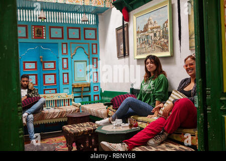 Due ragazze giovani e moderne seduti sul divano bevendo tè e bevande in un caffè a Medina Foto Stock