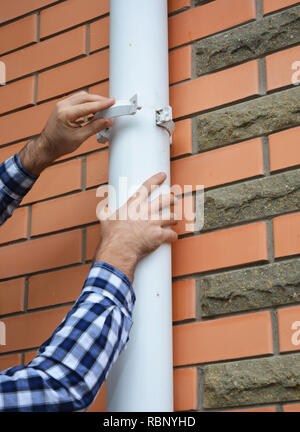 Contraente installazione e riparazione di pioggia in pvc sistema di gronda titolare di pipeline. Grondaie di plastica e drenaggio per tuttofare mani. Foto Stock